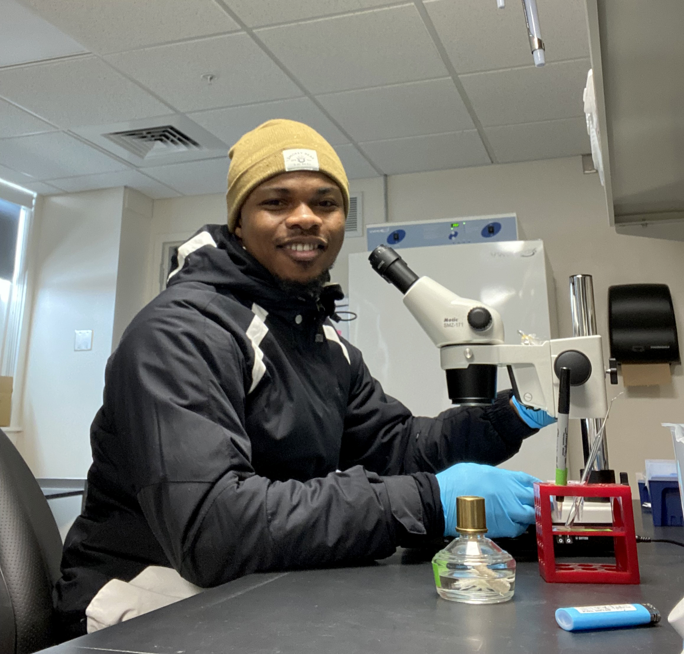 Kwaku Agyekum smiling at the camera, sitting in front of a microscope