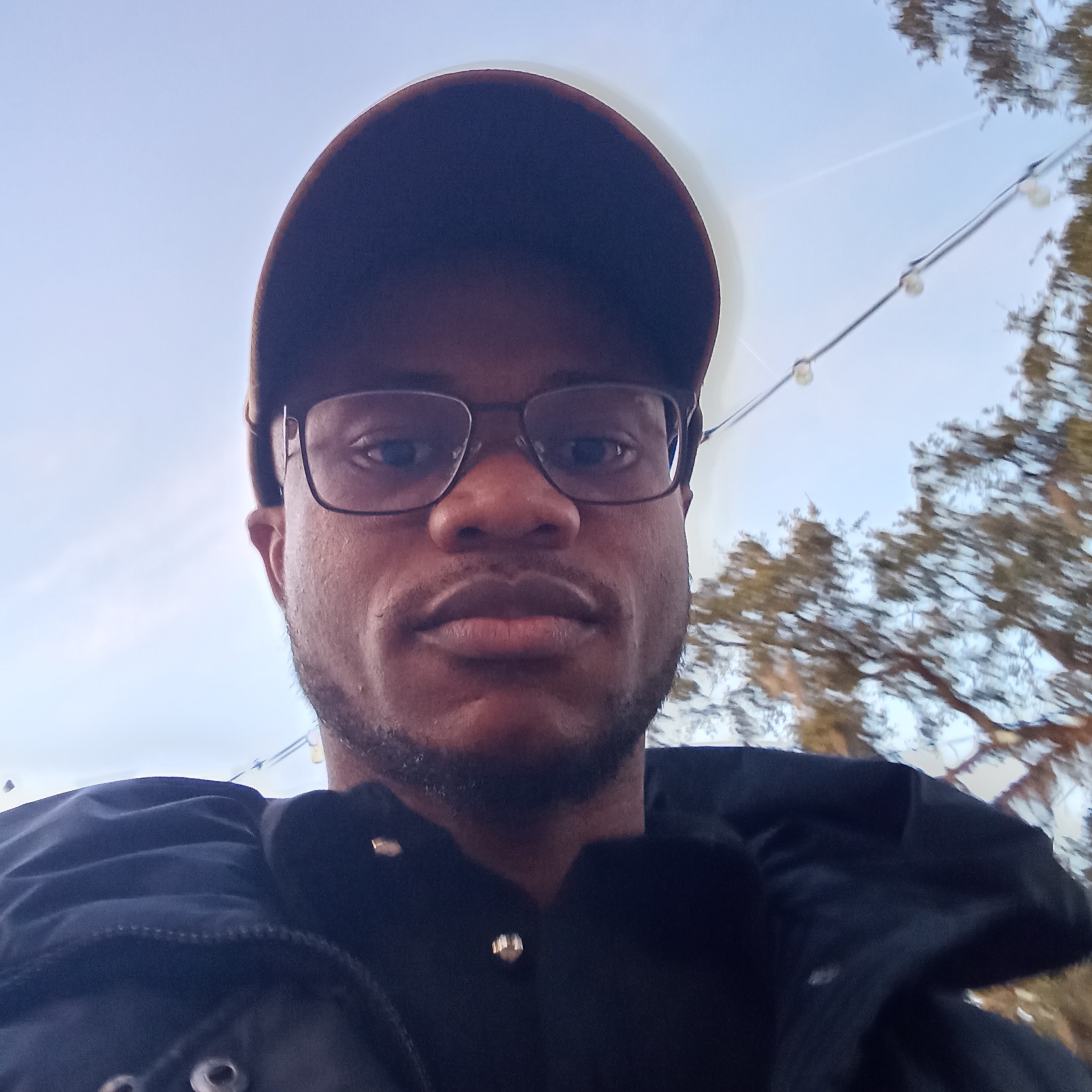 Cornelius Nichodemus closeup photo. He's looking down at the camera, wearing glasses and a baseball cap.