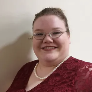 Teresa Easterbrooks headshot. Woman smiling, wearing glasses and a red dress with pearl necklace